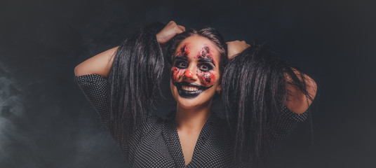 Smiling girl is playing a role of evil psycho clown with creepy makeup on her face.