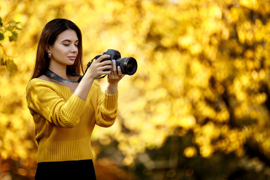 beautiful woman photographer with camera takes pictures in park in autumn. copy space