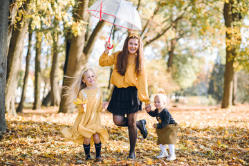Fototapeta premium mom with two little daughters in yellow clothes walking in the autumn park