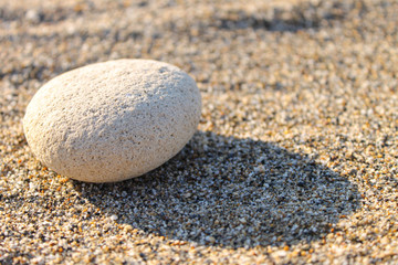 Fototapeta na wymiar One white pebble stone on the sand. Sunset photo with long shadows.
