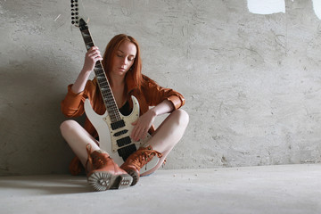 Young red-haired girl with an electric guitar. Rock musician girl in a leather jacket. She is a...