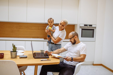FBeautiful family at home use laptop for working from home. White interior, white colors. In the kitchen