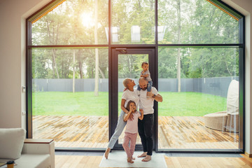 Beautiful and happy family together at home with panoramic window standing. Baby sit at daddy's...