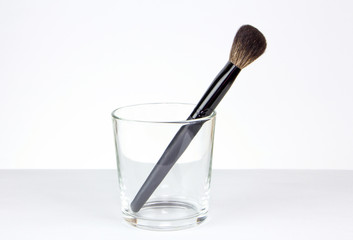 Black makeup brush with a long handle on a white background. Brush for blush and bronzer in a glass cup.