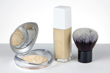 Set of foundation for the face on a white background. Shiny face powder, liquid base in a glass bottle and compact makeup brush.