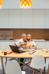 Happy caucasian couple resting, woman with phone. Happy Family at home, white interior, laptop on table. Male and Famale in kitchen. Smiling person