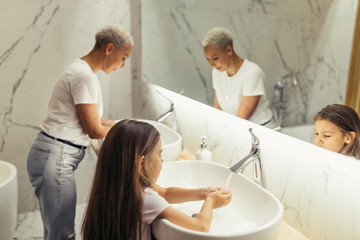 Young woman with her kid in bathroom washing hands with anti-bacterial soap. Morning together with child.