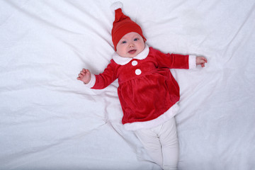 Portrait of displeased little baby in a santa hat and costume. Christmas concept. White bed.