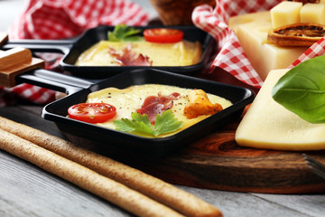 Delicious traditional Swiss melted raclette cheese on diced boiled or baked potato and baguette served in individual skillets with salami..