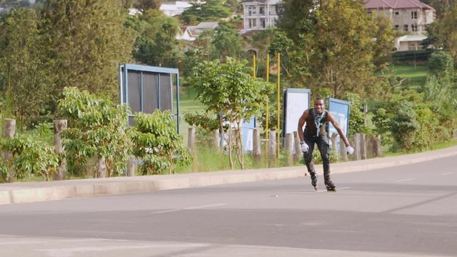 Attractive young african boy rollerblader entertaining people in the road doing different tricks slow motion wide view shot during midday in summer time
