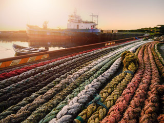 Multi colored ropes in a port, Close up selective focus,  Sun flare. Small fishing ship in the...