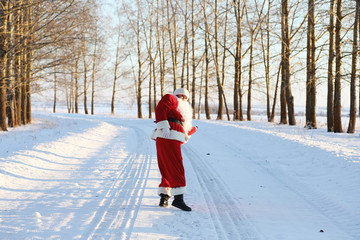 Santa in the winter field. Santa magical fog is walking along the field. Santa on Christmas Eve is carrying presents to children in a red bag.