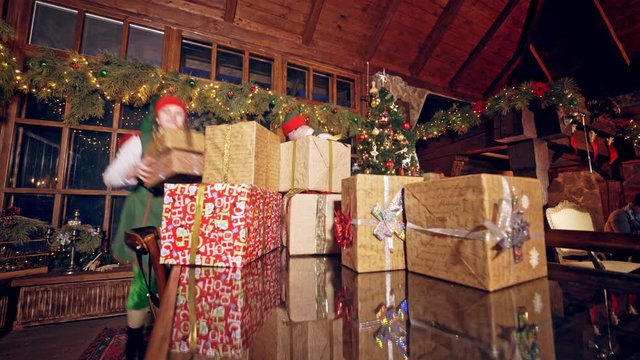 Gifts for Christmas on the table. Two happy elves putting presents on a desk at Christmas decorated room. Pile of boxes with presents for children.