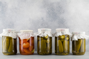 Pickled tomatoes and cucumbers in a glass jar on blue background.