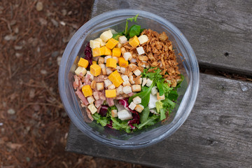 HEALTHY SALAD PLASTIC PACKED ON OLD WOODEN TABLE, DURING FOOD IN THE FIELD