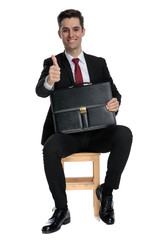 Cheerful businessman holding his briefcase and giving a thumbs up