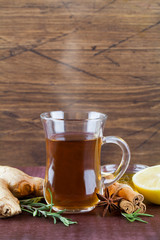 hot tea in glass cup with honey cinnamon lemon rosemary and ginger on wood background.