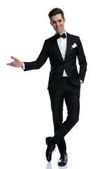 smiling elegant man in tuxedo inviting and presenting to side
