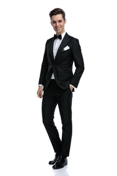 happy elegant man in tuxedo walking on white background