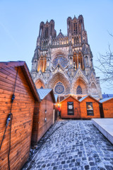 Illuminated warm Reims cathedral and Christmas market wooden houses in city center, France - 298735114