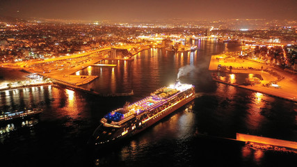 Aerial drone night shot of beautiful illuminated port of Piraeus and huge cruise liner departing to Aegean popular destinations, Attica, Greece