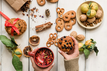 Hands of girl holding appetizing cupcake with blackcurrant and hot herbal drink