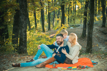 Fototapeta premium Picnic in nature. Happy family sitting together on a blanket hugging. Country style family. Meaning of happy family. United with nature.