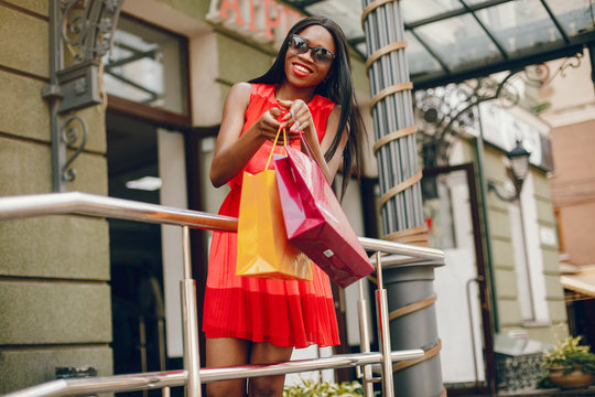 Black girl in a summer city. Woman with a shoping bags. Lady in a red ress