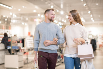 Cheerful young couple carrying paperbags while leaving clothing department