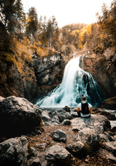 Young male hiker sitting on rocky shore of the waterfall, preparing for camping at this place. Male hiker enjoying in the nature with water.