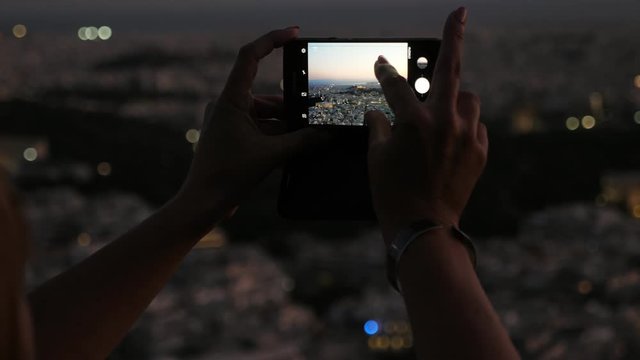 Female fingers keeping a phone and taking a photo of Athens cityscape at night 
