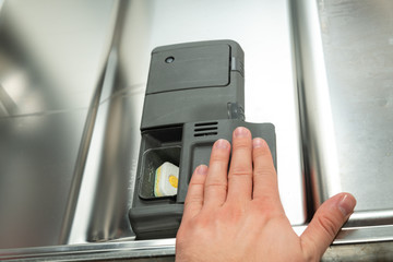 Loading the tablet into the dishwasher. The concept of using a dishwasher to wash dishes. A man puts the tablet in the dishwasher to wash dirty dishes.