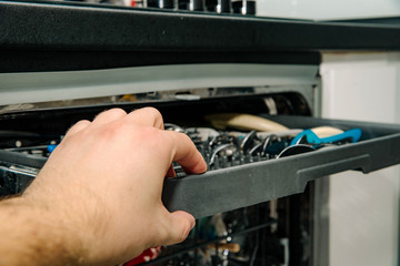 Opening the dishwasher. The concept of using a dishwasher to wash dishes. The man inserts open the dishwasher to put dirty dishes.