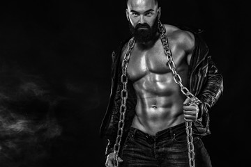 Men's fashion concept. Close-up portrait of a brutal bearded man topless in a leather jacket. Athlete bodybuilder on black background.