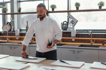 Handsome young chef African ethnicity lays knives on table in front of a culinary master class.