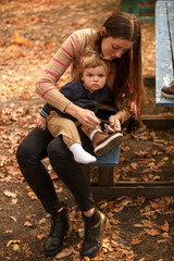 Naklejka na ściany i meble Beautiful mother tying shoes for baby. Autumn park. Mom and son. Lifestyle.