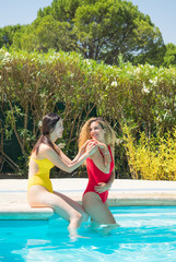 A chinese and a caucasian women sitting on the edge of the pool in affectionate attitude