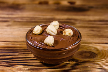 Obraz na płótnie Canvas Glass bowl with chocolate spread and hazelnuts on a wooden table