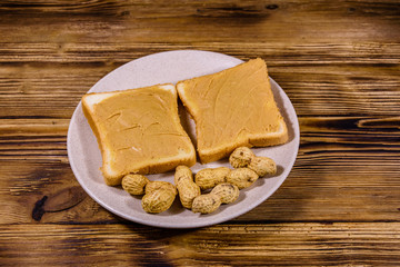 Glass jar with peanut butter and plate with sandwiches on a wooden table