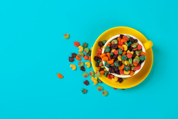 Yellow coffee cup with colorful cereals on bright turquoise background. Minimal food flat lay