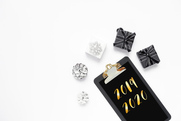 New year goal, plan, golden text 2019 2020 on black clipboard with paper blank, white, black gift boxes, pine cone on white backdrop. Motivation, inspiration concept idea, design flat lay, copy space