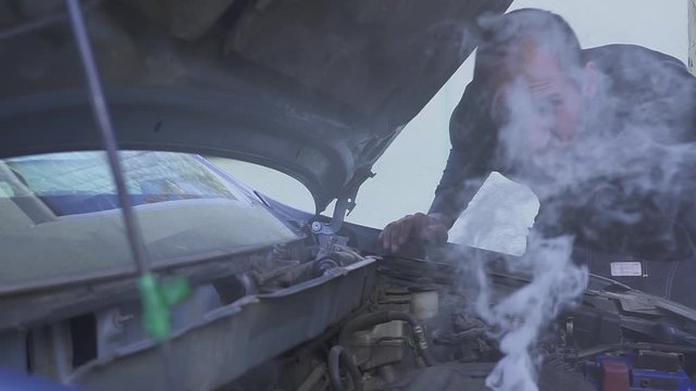 A man is very frustrated while trying to evaluate his smoking car engine.