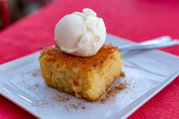 Piece of tasty vegan orange cake with vanilla ice cream served on white board