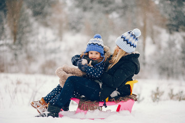 Family have fun in a winter park. Stylish mother in a black jacket. Little girl with pink sled