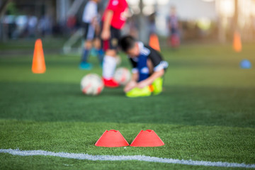 selective focus to marker cones are soccer training equipment on green artificial turf with blurry kid players training background. material for training class of football academy.