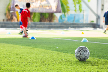 Soccer ball on green artificial turf with blurry soccer team training. Blurry kid player training and soccer equipment in soccer academy.
