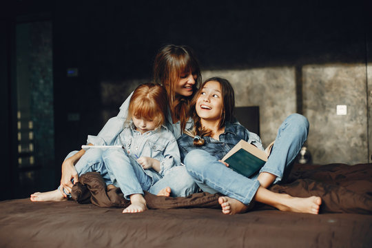 Beautiful mother with two daughter. Family sitting in the room on a bed. Girl reading a book