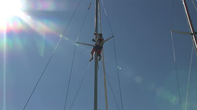 Man rises on mast of yacht on background of blue sky and sun while teaching yachting in school of captains. Marine equipment on sailing boat in regatta.