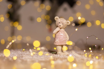 Decorative figurines of a Christmas theme. Figurine of a cute teddy bear girl in a sweater with deers. Festive decor, warm bokeh lights.