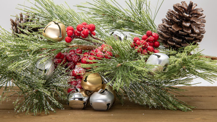 Seasonal holiday green fir with gold, silver, and chrome bells on white background with Holly berry, pine cone, and snow.